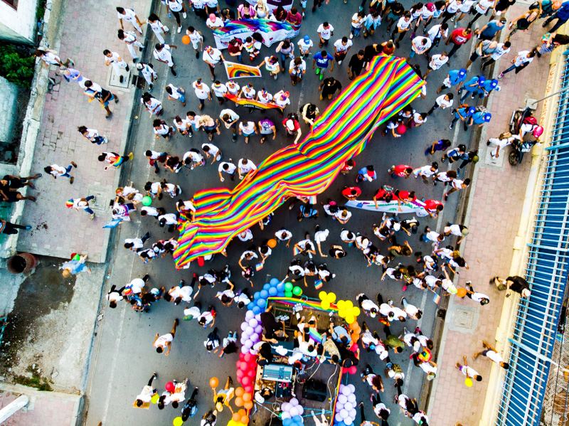 Aerial view of a crowd carrying a rainbow banner through a street